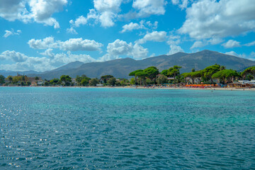 Blick über das türkisblaue Meer auf den Strand von Mondello mit seinen Bergen im Hintergrund und blauem Himmel mit vielen kleinen Wolken.