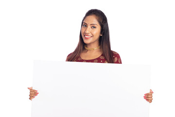 Cheerful Indian young woman holding white board on white background.