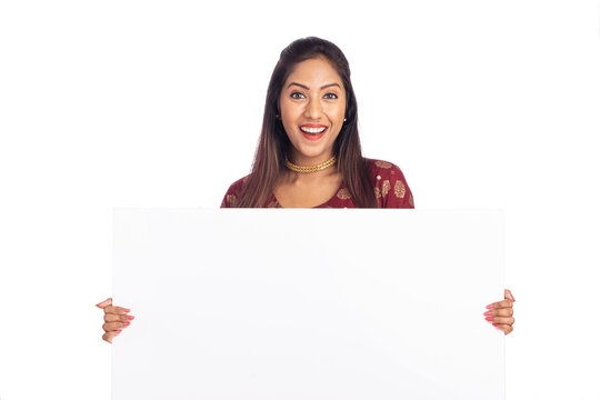 Cheerful Indian young woman holding white board on white background.