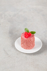Vegan dessert. Red plum mousse cream cake of cylindrical shape, on a plate. Light grey background. Copy space