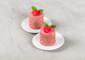 Red plum mousse cake of cylindrical shape, on a plate. Light grey background
