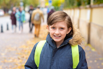 Fototapeta premium portrait of a happy schoolboy in a jacket with a backpack going to school in autumn