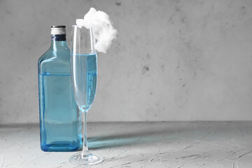Bottle and glass with tasty cotton candy cocktail on grey background