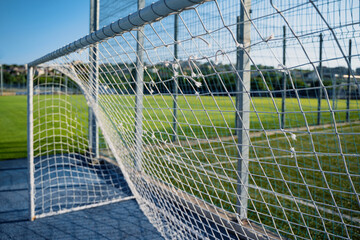 closeup of soccer gate goalpost white rope net with green field in background