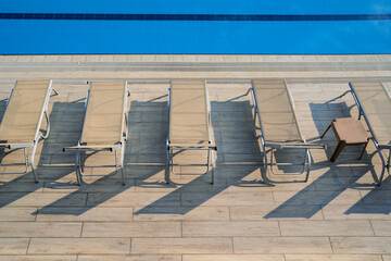top view row of sunlounger chairs near a outdoor swimming pool with blue water