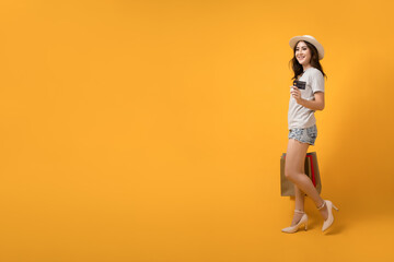 Beautiful Asian shopaholic woman smiles and happy while carrying shopping bags and credit card on yellow background. Summer sale, Mid-year sales concept. - obrazy, fototapety, plakaty
