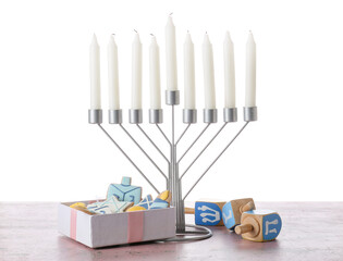 Menorah with candles, dreidels and gift box with cookies for Hanukkah celebration on table against white background