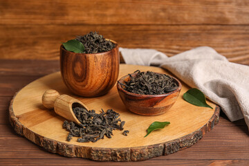 Bowls and scoop with dry tea leaves on wooden background