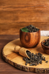 Bowl and scoop with dry tea leaves on wooden background