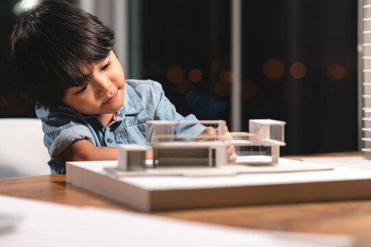 Inspiration kids in occupation in the future, Asian kid playing and concentrating to home model box in the job of parent at office room at night. Skill and learning practice of children's success.