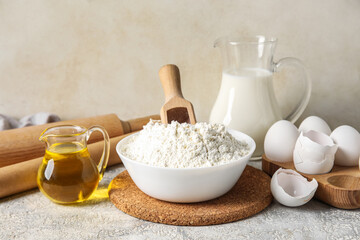 Bowl with flour and ingredients for baking on light background