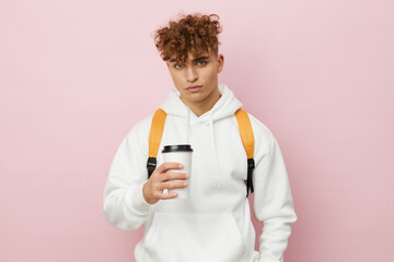 a nice man is standing on a pink background in a white hoodie with a backpack on his back and holding a glass with a drink in his hand