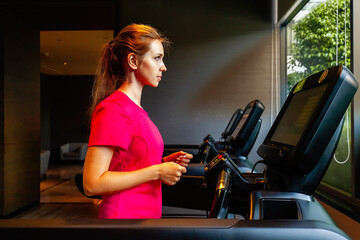 Fototapeta na wymiar Young woman in sportswear running on treadmill in modern gym