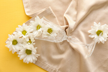 Glass, napkin and chamomile flowers on yellow background