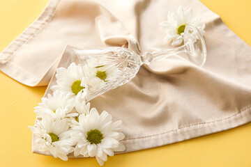 Glass, napkin and chamomile flowers on yellow background