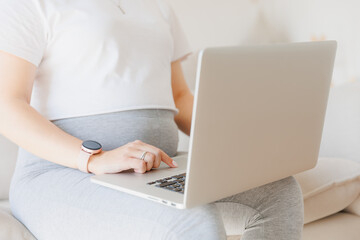 Closeup hand of pregnancy woman using online laptop on sofa with sunlight