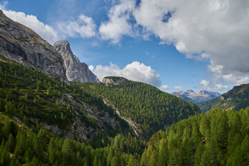 Fototapeta na wymiar High rocky mountains, green hills and blue cloudy sky at spring, Italian Alps, Italy, Europe
