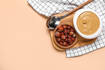 Wooden board with bowl of tasty hazelnut butter and nuts on color background