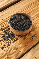 Bowl of black sesame seeds on wooden background