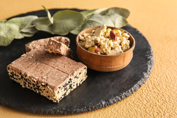Slate board with tasty sesame halva with pistachios on color background, closeup