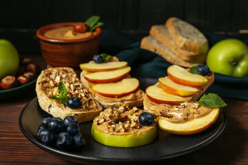Fototapeta na wymiar Plate of tasty sandwiches with nut butter, apples and blueberry on wooden table, closeup