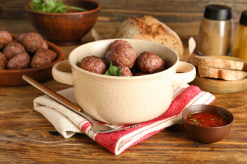 Cooking pot with tasty meat balls, napkin, sauce and fork on wooden background