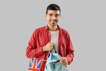 Young man with UK flag and backpack on grey background