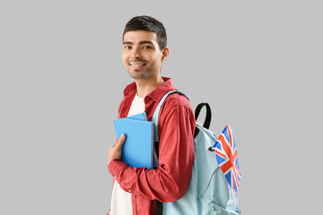 Young man with UK flag, books and backpack on grey background