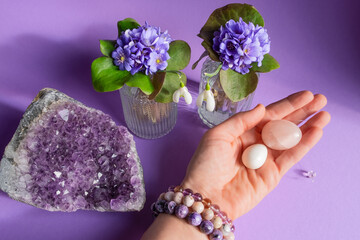 Woman hand in stone bracelets on purple background holding two yoni eggs