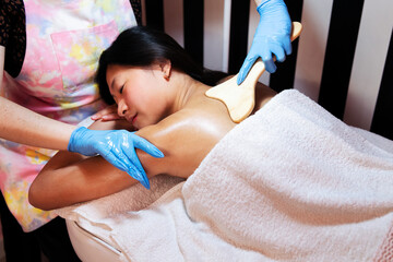 young woman relaxes lying on the beauty salon table while receiving a relaxing shoulder massage with a wooden spatula, concept of body care and wellness