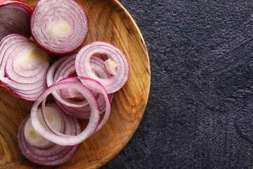 Wooden plate with cut red onion on dark background, closeup