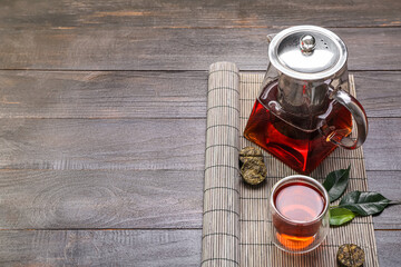 Bamboo mat with teapot and glass of puer tea on dark wooden background