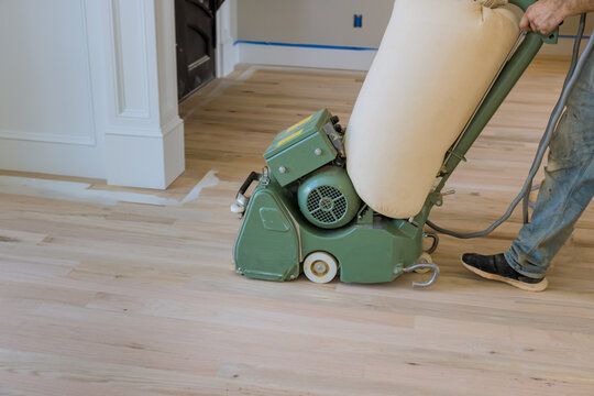 Process of grinding wooden parquet floor with floor sander in new house when it has just been constructed