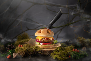 Halloween burger in a shape of pumpkin head jack lantern in a mystery forest. Scary cheeseburger on...