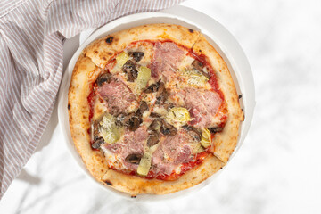 Pizza capricciosa with white mushrooms, ham, artichoke, tomatoes, olives, parmesan and mozzarella on white background for restaurant