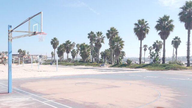 Basketball court with hoop, net and backboard for basket ball game on beach, California coast, USA. Sport field for streetball or netball players, palm trees on ocean shore. Mission beach, San Diego.