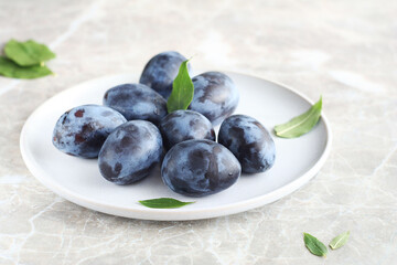 A ripe plum lies in a light plate on a marble table. green leaves scattered around