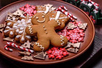 Beautiful gingerbread on a brown ceramic plate with Christmas tree decorations on a dark concrete background