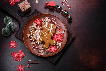 Beautiful gingerbread on a brown ceramic plate with Christmas tree decorations on a dark concrete background