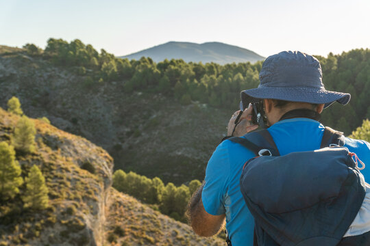 Rear view, hiker man with backpack taking photos at mountain landscape