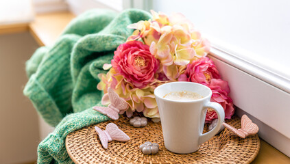 Home composition with a cup of coffee, flowers and a knitted element.