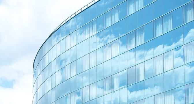 Tall generic corporate office building exterior, square glass windows reflecting clouds, bright white blue wide slide background, copy space, nobody. Modern business architecture, cloud reflections