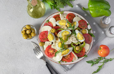 Healthy salad with tomatoes, mozzarella, olives, arugula and eggs on plate on light gray background