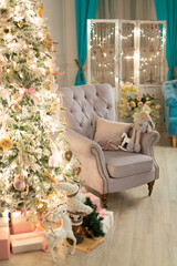 gray armchair stands near the Christmas spruce decorated with a luminous garland and toys