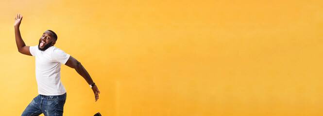 Fototapeta na wymiar Full length of handsome young black man jumping against yellow background.