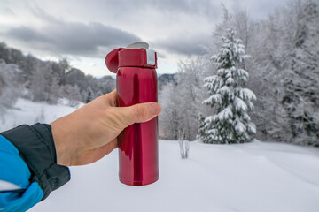 Red thermo bottle for winter leisure. Flask thermos of drinks in hand on background of winter mountains landscape