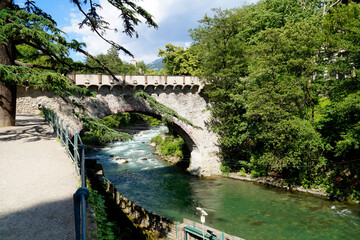 the picturesque mediterranean town of Merano with an ornate stone bridge over the emerald-green...