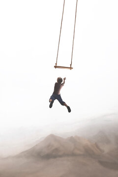 surreal jump of a boy trying to hang himself in a swing that twirls in the sky, concept of risk and success