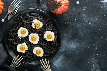 Halloween party Italian black pasta decorated horror  olives like eyes on black plate on old dark table background. Monster face from pasta. Halloween decorations and Halloween food concept. Mock up.