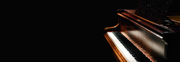 A wide photo of a real wooden classical acoustic grand piano made of wood isolated against a dark black background with copy space for a custom message - obrazy, fototapety, plakaty